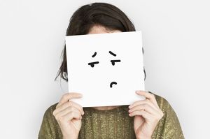 へこんだ顔が書いてある紙をもつ女性