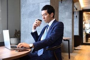 コーヒーを飲みながらパソコンを操作するスーツ姿の男性