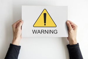 「!」「WARNING」と書かれた紙を持つ手