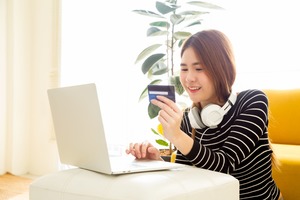 ノートパソコンの前でカードをみながら微笑む女性