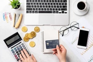 ノートパソコンとスマホ置きクレジットカードを持ちながら電卓をたたく手元