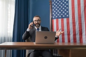 アメリカ国旗とノートパソコンとスマホで話す男性